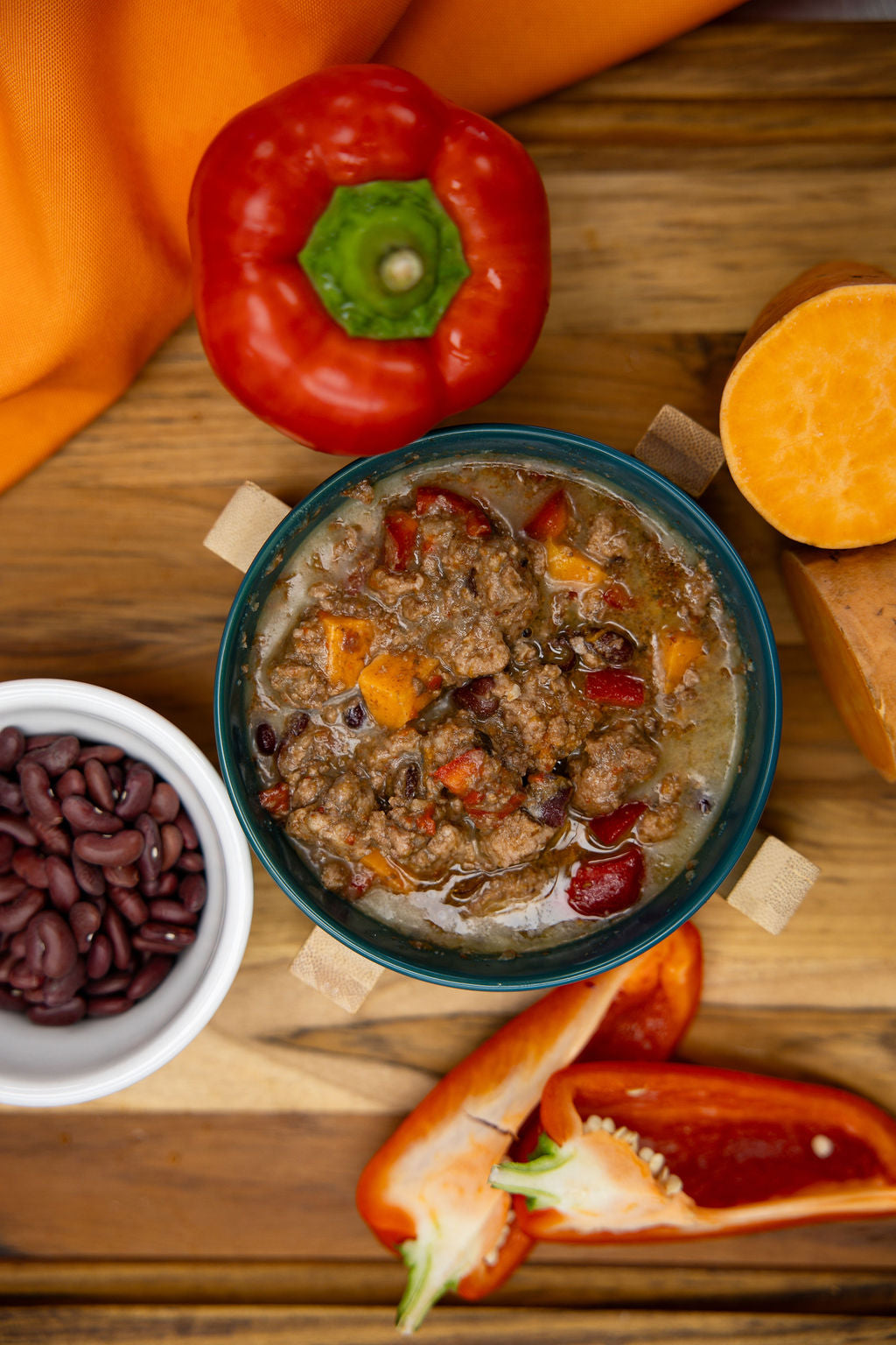 Bowl of stew with red and orange bell peppers, sweet potatoes, and beans on a wooden surface.