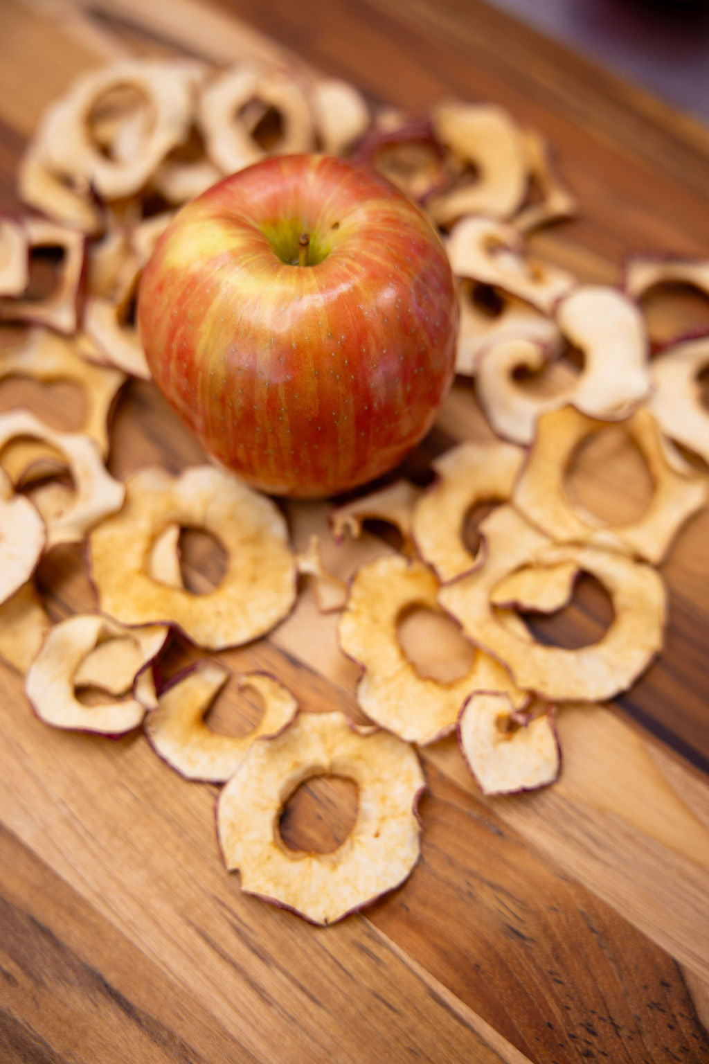 Whole apple surrounded by dried apple slices on a wooden surface