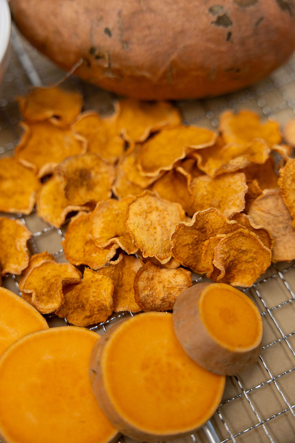 Dried sweet potato slices on a wire rack with a whole sweet potato in the background.