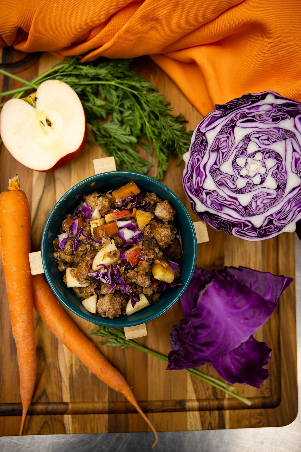 Dish with roasted vegetables on a wooden board with carrots, apples, and purple cabbage.