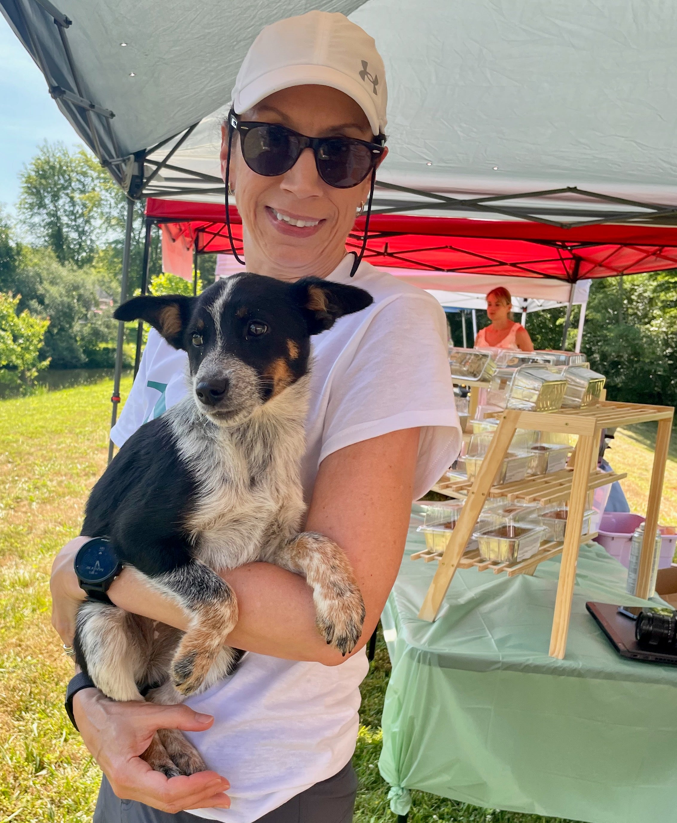 Person holding a puppy outdoors under a tent with a table in the background